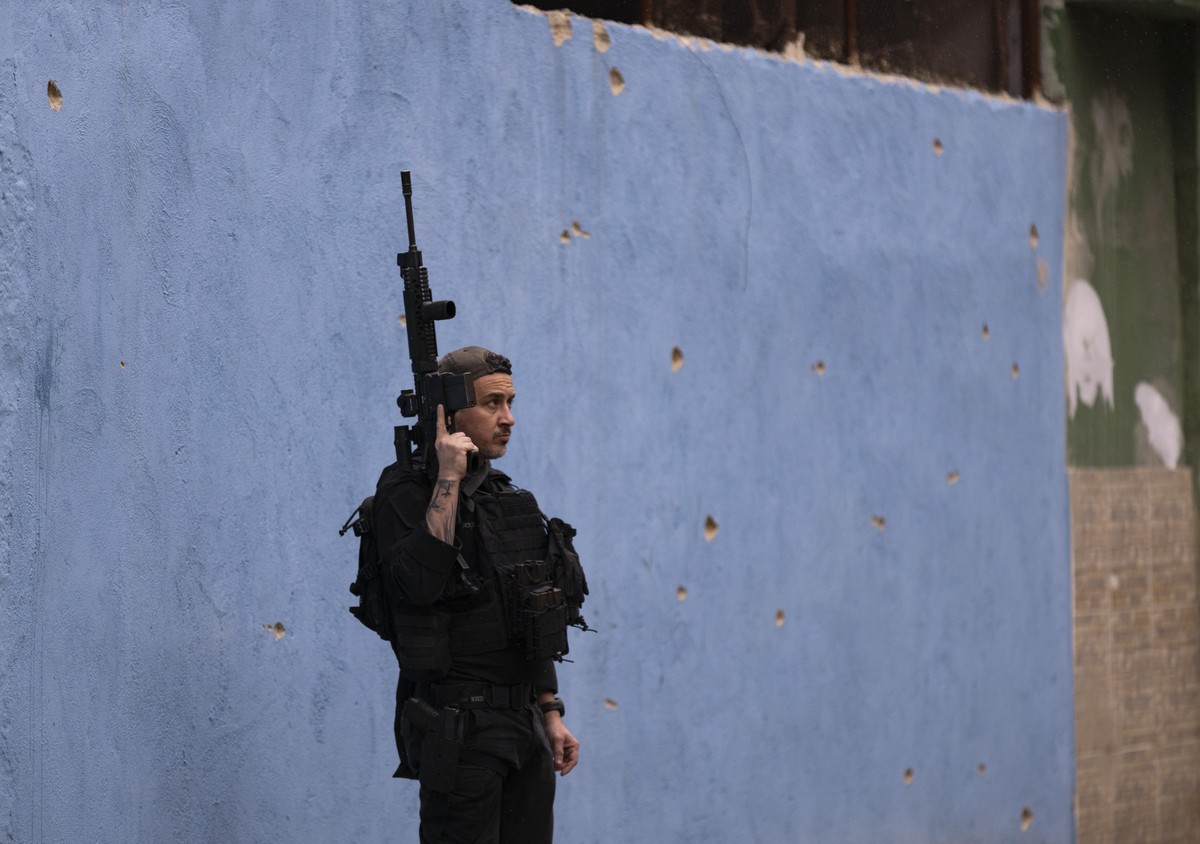 MPF solicita plano de reposição de aulas canceladas por violência em 120 dias Policial armado diante de parede de escola em Parada de Lucas, no Rio, com marcas de bala (Foto: Márcia Foletto)
