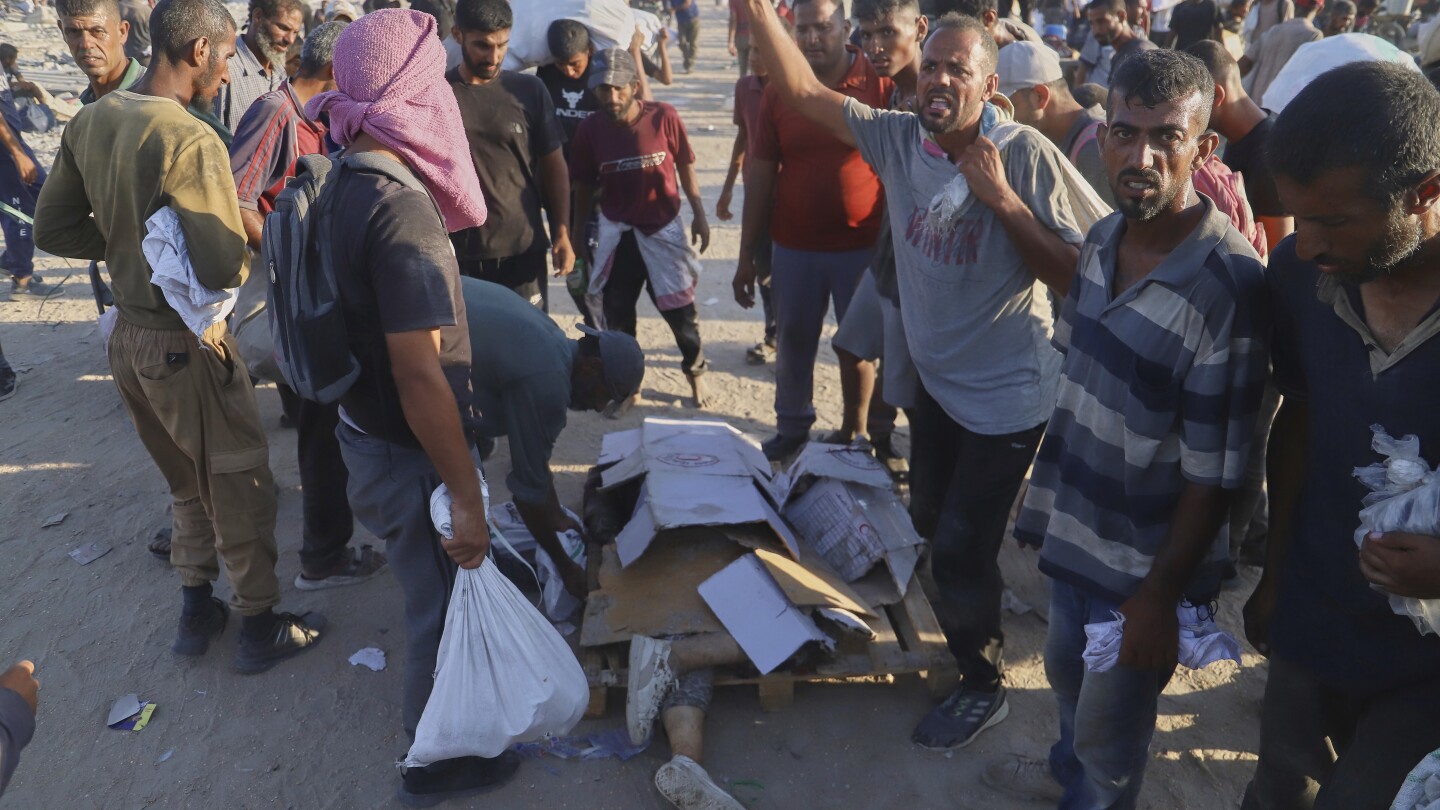Palestinos ficam ao lado do corpo de uma mulher que foi atropelada por um caminhão enquanto tentava alcançar um comboio de ajuda humanitária que se movia ao longo do corredor de Morag, perto de Rafah, na faixa de Gaza, sul, na segunda-feira, 4 de agosto de 2025. (Foto: AP Photo/Mariam Dagga)