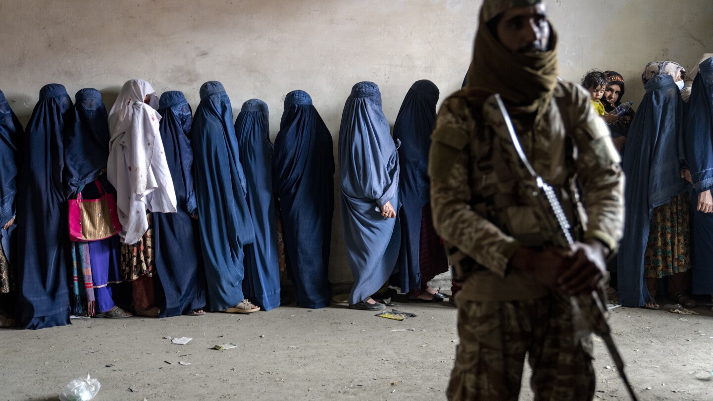 Um combatente do Talibã faz a guarda enquanto mulheres aguardam para receber rações alimentares distribuídas por um grupo de ajuda humanitária em Cabul, Afeganistão, em 23 de maio de 2023. (Foto: AP Photo/Ebrahim Noroozi, File)