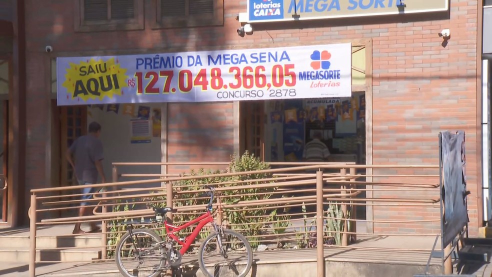 Família é ameaçada após vizinho espalhar boato sobre prêmio da Mega Sena Faixa pendurada na lotérica Mega Sorte, em Matozinhos, anuncia vencedor do prêmio de R$ 127 milhões (Foto: Reprodução/TV Globo)