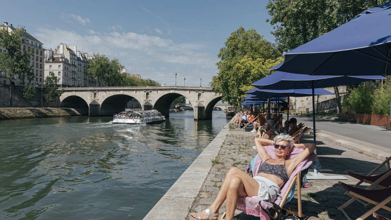 Paris transforma o Sena em uma praia tropical com cores brasileiras Uma mulher tomando banho de sol em uma praia artificial nas margens do Rio Sena, em Paris. 14/08/2023 (Foto: Andrea Mantovani/Bloomberg/Getty Images)