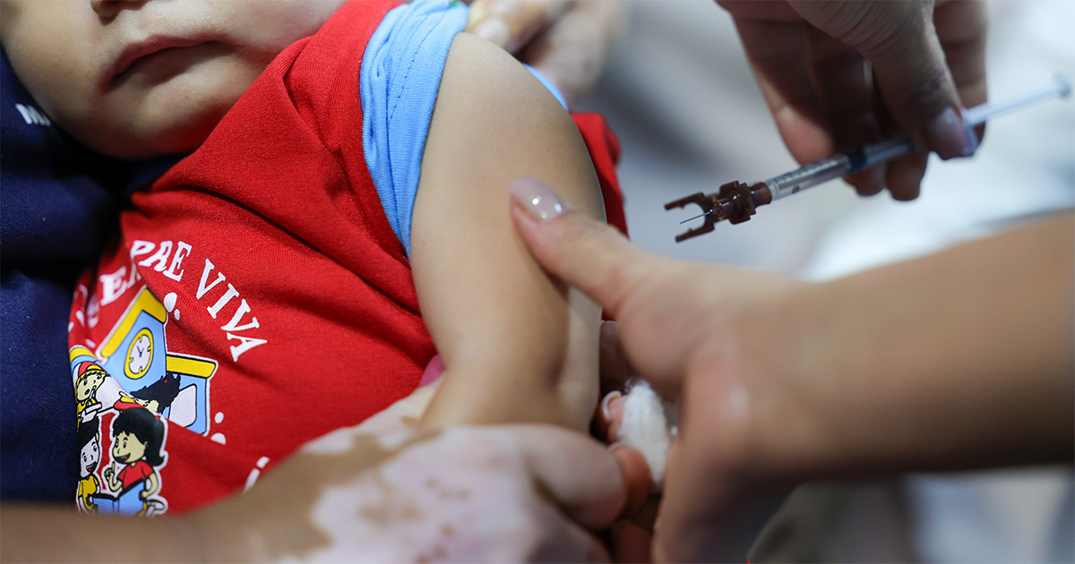 Criança olha para uma enfermeira que se prepara para aplicar uma vacina (Foto: USP Imagens)